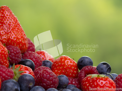Image of Pile od strawberries, blueberries, raspberries on green background