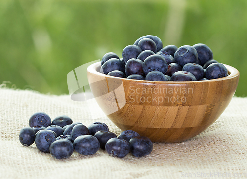 Image of Blueberries in a wooden bowl on a rustic table with green background