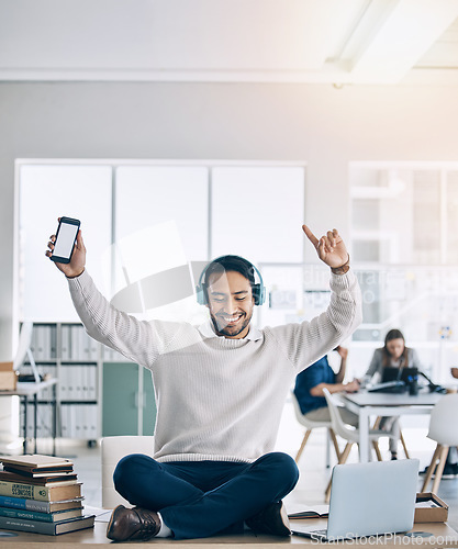 Image of Music, phone and businessman with headphones on desk listening to audio, track and radio in office. Freedom, happiness and man sitting on table in corporate workplace with mockup smartphone screen