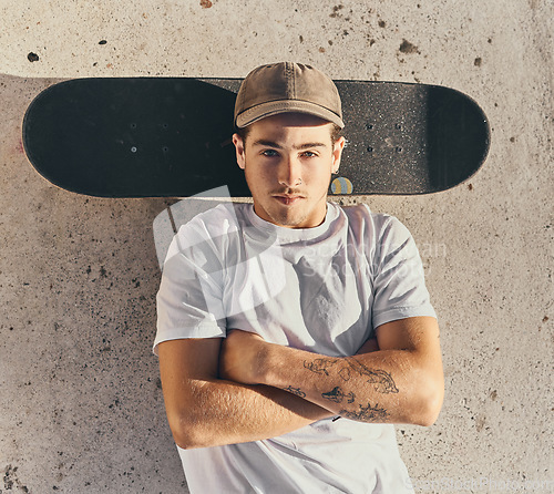 Image of Skateboard, fashion or man with arms crossed in city skate park for stunt training, hobby exercise or freestyle skating in top view. Portrait, skater or skateboarder lying on concrete ground or floor