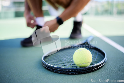 Image of Tennis ball, racket and man tie shoes on tennis court preparing for competition, game or match. Exercise, fitness and tennis player getting ready for practice, training or workout outdoors on field.