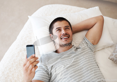 Image of Man, happy and thinking with a phone on a bed for communication, chat or notification at home. Young person relax with a smartphone and an idea for internet connection, app or social media message