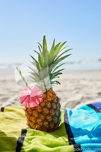 Image of Cocktail, travel and closeup of a pineapple on a beach with alcohol on a towel for vacation. Summer, ocean and tropical organic fruit with a straw or paper umbrella on the sand for a seaside holiday.