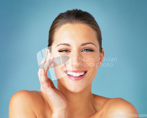Image of Dermatology, portrait and happy woman with cream on face, cosmetics and product for makeup on blue background. Happiness, skincare and wellness for model with smile, beauty and lotion for facial glow