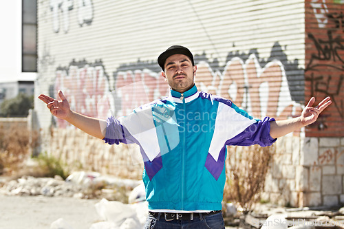 Image of Graffiti artist, city and portrait of man in street stand by art, illustration and creative wall design. Fashion, gangster and person with hand sign in trendy, urban streetwear and casual clothes