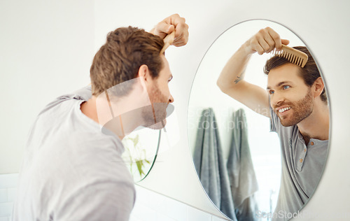 Image of Bathroom mirror, reflection and happy man brush hair for growth maintenance, beauty routine or hygiene cleaning treatment. Smile, morning and home person with bamboo comb for rich healthy hairstyle