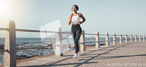 Image of Fitness, woman run at beach and with headphones listening to music for health wellness. Training or exercise, marathon or lens flare and female person running along the promenade listen to radio