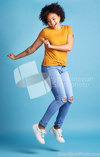 Image of Excited, happy or woman celebrate, jumping or winning with opportunity, energy or dancing. Female person, model or girl in the air, dance or excitement with victory or fun on a blue studio background