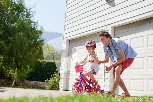 Image of Father teaching child to ride a bike as support, trust and skill development outdoor of a home or house together. Parent, safety and happy dad care and help kid or girl learning to use a bicycle