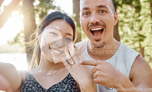 Image of Couple, engagement and ring in selfie with smile, excited face and pointing for memory in forrest. Young man, happy woman and jewellery for proposal, marriage offer and photography for social network