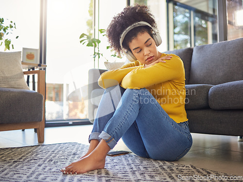 Image of African woman, sad and headphones on floor with worry, stress or memory of trauma in home living room. Gen z girl, anxiety and remember mistake, regret or mental health with music in apartment lounge