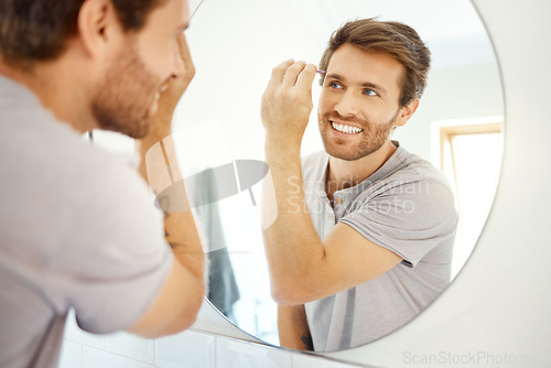 Image of Man, tweezer and eyebrow in bathroom mirror with smile, self care and hygiene to start morning in home bathroom. Young guy, person and tool for beauty, facial cosmetics and wellness for hair removal