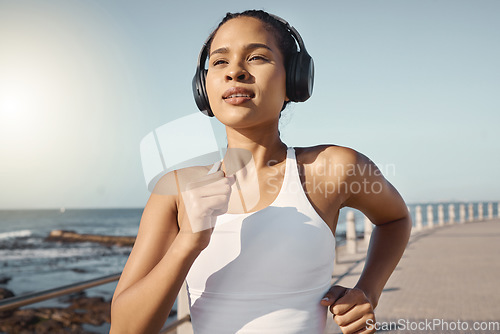 Image of Fitness, woman run at beach and with headphones listening to music for training. Exercise or marathon, lens flare or sportswear and female athlete running along the promenade listen to radio
