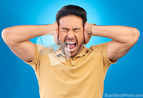 Image of Man covering his ears while screaming in a studio for angry, upset or mad argument expression. Crazy, shout and young male person with an open mouth for loud voice gesture isolated by blue background