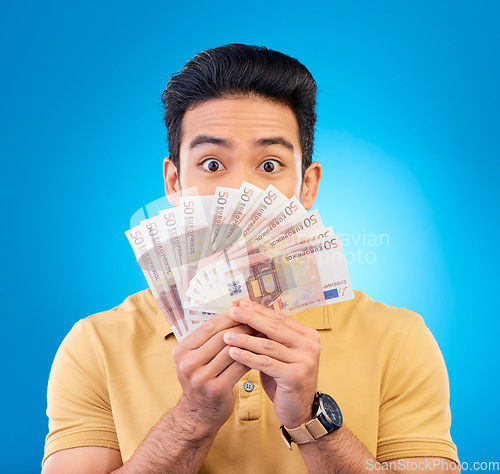 Image of Money, fan and man with wow face isolated on blue, studio background for winning, cash surprise or financial profit. Lottery, gambling secret and asian person winning, bonus and cashback in portrait