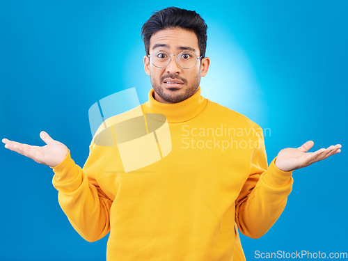 Image of Confused, shrug and portrait of a man in a studio with an unsure, doubt or question expression. Uncertain, choose and headshot of a male model with a decision gesture isolated by a blue background.