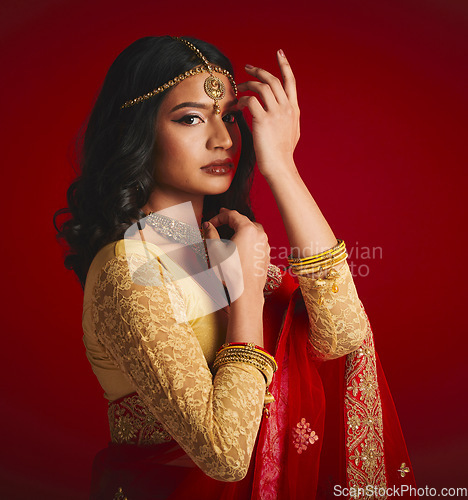 Image of Portrait, celebration and Indian woman with fashion, traditional dress and jewellery against a red studio background. Face, female person or model with cultural clothes, religion and beauty with gold