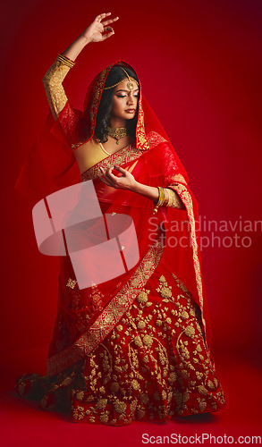 Image of Fashion, dancing and Indian woman in a traditional dress, celebration and confident on a red studio background. Female person, girl and model with a cultural outfit, dancer and ritual with confidence