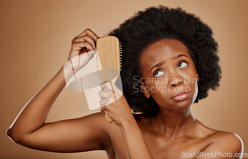 Image of Black woman, hair care and worry with brush in studio, brown background and curly afro. Beauty, sad female model and comb tangled knot in hairstyle with anxiety, stress and unhappy with dry texture