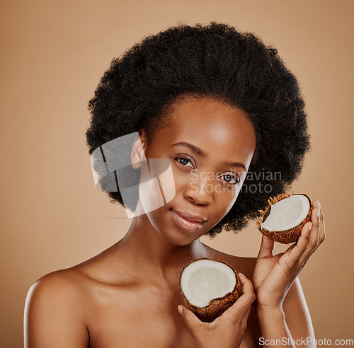 Image of Portrait, facial and coconut with a model black woman in studio on a brown background for natural treatment. Face, skincare or luxury beauty cosmetics with a young female person holding fruit for oil