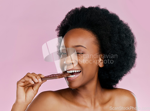 Image of Black woman, eating chocolate and diet with candy and beauty, health and dessert snack on pink background. Skin, glow and female model wink with cacao sweets, calories and cosmetics in studio