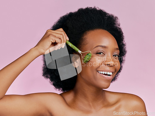 Image of Happy, skincare and portrait of black woman with a jade roller for a facial massage or treatment. Smile, relax and African girl or model with a facial product isolated on a pink background in studio