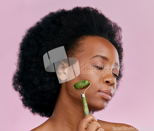 Image of Facial roller, massage and black woman with natural beauty, face care and skin glow on pink background. Female model, cosmetic tools and dermatology with jade crystal, afro hairstyle and skincare