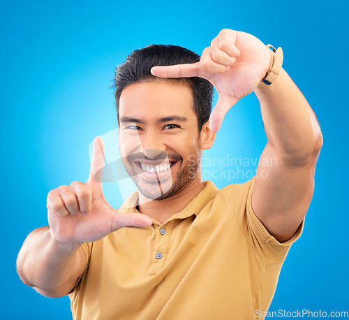 Image of Portrait, finger frame and man in studio, blue background and review profile picture. Face, happy asian model and hands for planning perspective of photography, selfie and inspiration of photographer