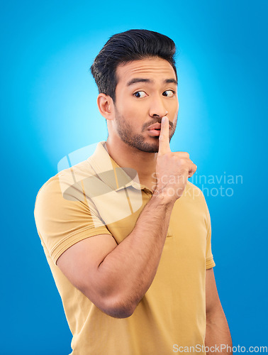 Image of Asian man, secret and finger on lips in studio for privacy, mystery and sale announcement on blue background. Male model, silence and shush for quiet, gossip or whisper emoji of confidential surprise