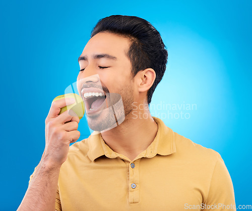 Image of Hand, man eating an apple and against a blue background for healthy diet. Nutrition or mockup space, isolated or green food and male person eat fruit for health wellness against a studio backdrop