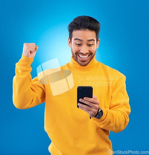 Image of Winner, surprise and excited Asian man with phone in studio for online bonus, competition and prize. Success, smartphone and happy male person on blue background for promotion, winning and good news