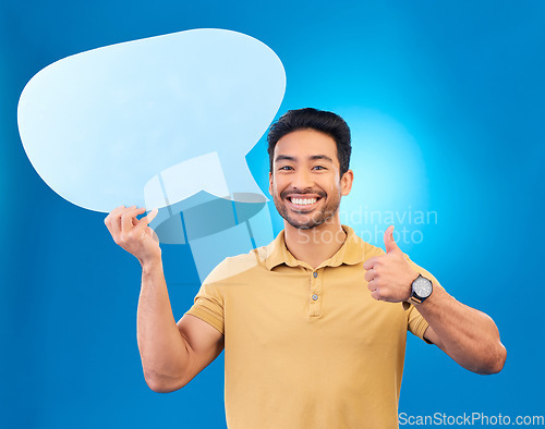 Image of Young man, speech bubble and studio portrait for thumbs up, opinion and social network by blue background. Indian guy, student or model for yes icon, mock up space and cardboard sign for promotion