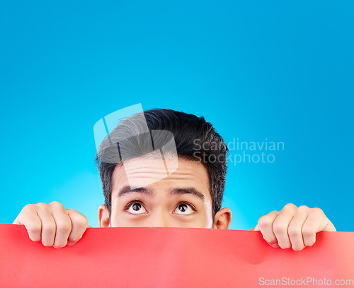Image of Eyes, poster and mockup with a man hiding in studio isolated on a blue background for advertising information. Space, sign and a male brand ambassador showing an empty placard for a marketing logo