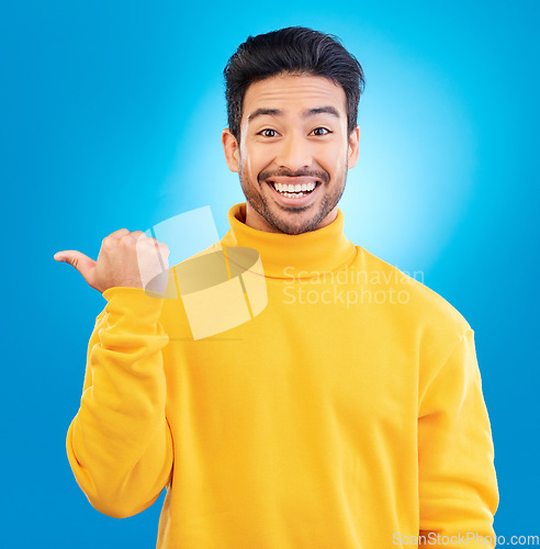 Image of Portrait, man and pointing to advertising space in studio, blue background and mockup of deal, promotion or news. Happy asian, male model and presentation of announcement, information or opportunity