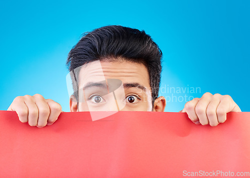 Image of Portrait, poster and mockup with a man hiding in studio isolated on a blue background for advertising information. Eyes, sign and a male brand ambassador showing empty space for a marketing logo