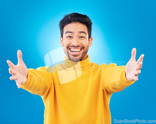 Image of Portrait, welcome and arms outstretched with a man on a blue background in studio for a friendly hug. Smile, trust and hello with a happy young male person reaching indoor to offer a greeting