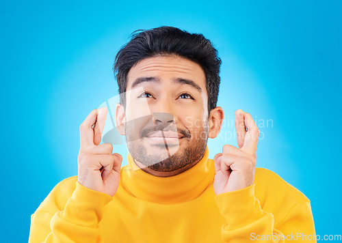 Image of Hope, man with his fingers crossed for luck and against a blue background for thinking. Praying or miracle, trust and male person with hand emoji for aspiration or idea against a studio backdrop.