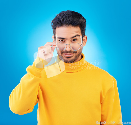 Image of Cool, fashion and portrait of a man with glasses, confidence and winter aesthetic. Sexy style, trendy and a fancy Asian model with fashionable eyewear isolated on a blue background in a studio