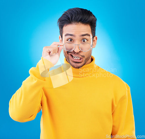 Image of Portrait, glasses and funny face with a man on a blue background in studio for vision or comedy. Comic, humor and fashion with a silly male person joking in prescription frame lenses or eyewear
