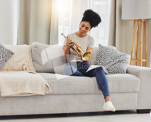 Image of Happy, woman and learning notes on trumpet in home for music, practice and classic jazz song. Young female person, musician and brass horn instrument on sofa, living room and hobby of musical talent