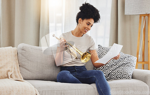 Image of Woman, music sheet and trumpet in home for learning, practice and classic jazz song. Happy young female person reading paper notes for brass horn instrument, hobby and musical talent in living room