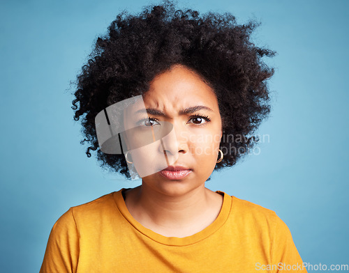 Image of Portrait, frown and anger with an african woman on a blue background in studio looking mad or serious. Face, bad or negative and an unhappy young female person with an afro feeling frustrated