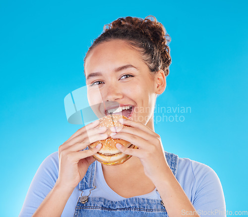 Image of Burger, smile and woman eating fast food and happy with lunch meal with a smile isolated in a studio blue background. Breakfast, craving and portrait of young female person enjoy snack or sandwich