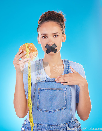 Image of Burger, diet and woman tape mouth for fast food and weight loss gives bad, disgust and frustrated review for protection. Disaster, mistake and person disappointed isolated in a studio blue background