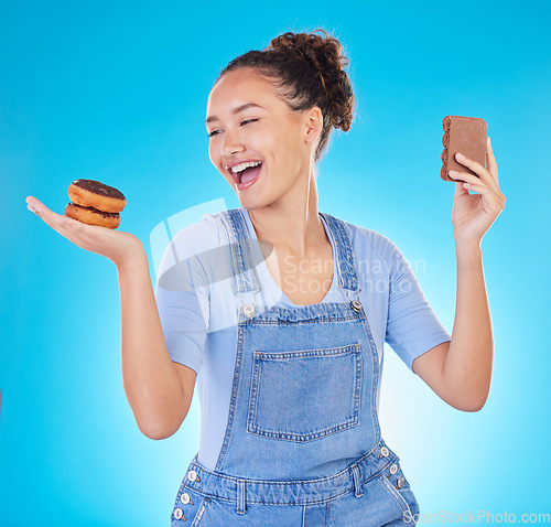 Image of Food, diet and happy woman with sweets in studio, chocolate and donut for eating plan on blue background. Health, nutrition and choice to lose weight, girl with smile and freedom for sugar or dessert