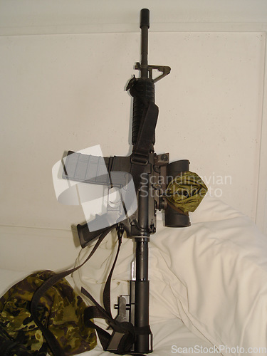 Image of War, camouflage and a rifle on a bed in the home of a soldier ready for conflict, battle or fighting. Army, military or weapon leaning against a wall in an apartment for self defense or patriotism