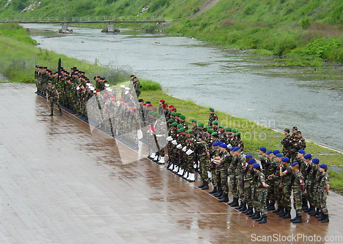 Image of Military, training or bootcamp with people in the rain for a drill at a parade as a special forces squad. Army, soldier and a group of personnel in camouflage uniform at attention by a river