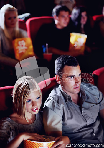 Image of Cinema, date and couple with popcorn, watching film or eating on romantic night together. Movie, man and woman in theater with snacks, show and sitting in auditorium to relax in evening with partner.