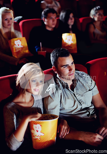 Image of Cinema, love and couple with popcorn, watching film or eating on romantic date together. Movie night, man and woman in theater with snacks, romance and sitting in auditorium to relax at show premier.