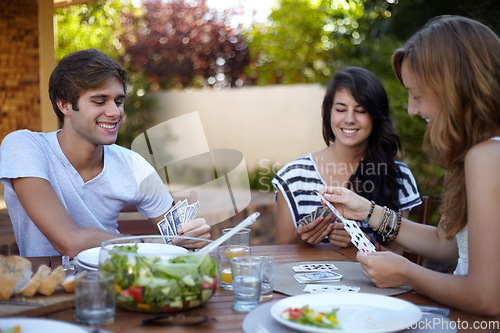 Image of Friends, card game and food in backyard for lunch and discussion with a smile and fun. Salad, laughing and young people outdoor of a home with communication and funny joke together with a meal